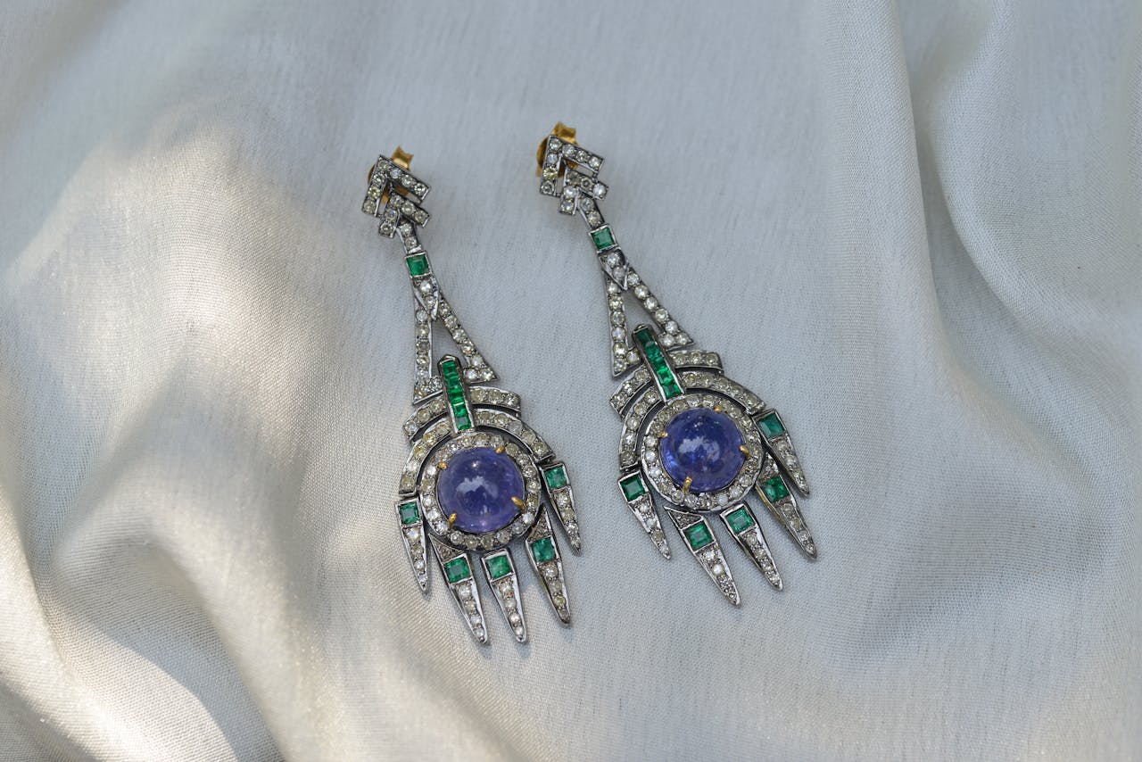 Close-up of luxurious Art Deco earrings with diamonds and gemstones on silky fabric background.